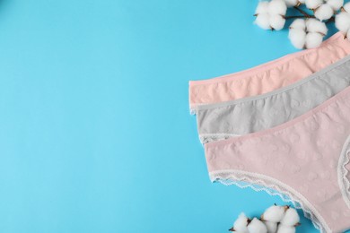 Photo of Women's underwear. Beautiful panties and cotton flowers on light blue background, flat lay. Space for text