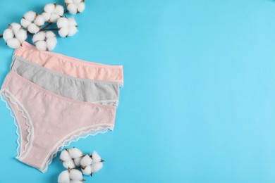 Photo of Women's underwear. Beautiful panties and cotton flowers on light blue background, flat lay. Space for text