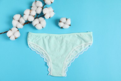 Photo of Women's underwear. Beautiful panties and cotton flowers on light blue background, flat lay