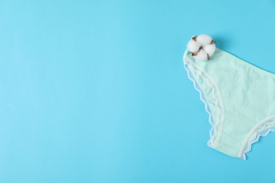 Photo of Women's underwear. Beautiful panties and cotton flower on light blue background, top view. Space for text
