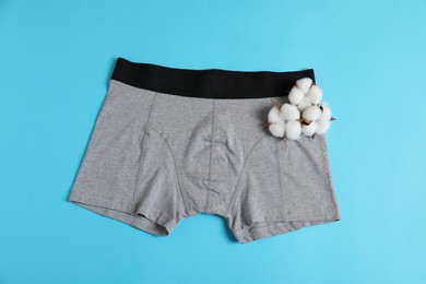 Photo of Comfortable gray men's underwear and cotton flowers on light blue background, top view