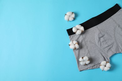 Photo of Comfortable gray men's underwear and cotton flowers on light blue background, flat lay. Space for text
