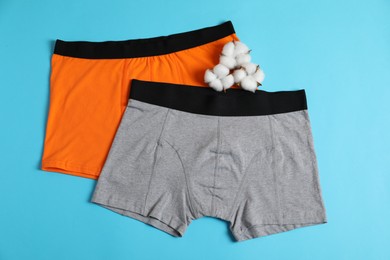 Photo of Comfortable men's underwear and cotton flowers on light blue background, top view