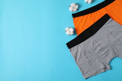 Photo of Comfortable men's underwear and cotton flowers on light blue background, flat lay. Space for text