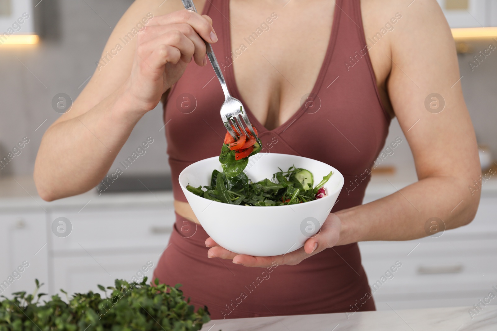 Woman in fitness clothes with salad indoors, closeup Photo of Woman in fitness clothes with salad indoors, closeup