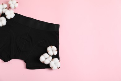 Photo of Comfortable black men's underwear and cotton flowers on pink background, top view. Space for text
