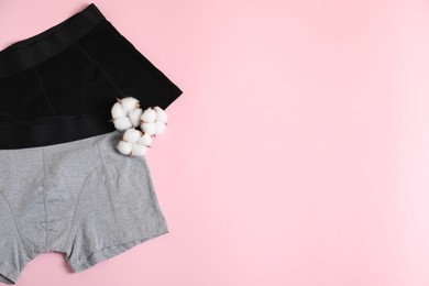 Photo of Comfortable men's underwear and cotton flowers on pink background, top view. Space for text