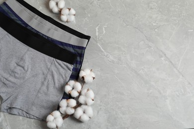 Photo of Comfortable men's underwear and cotton flowers on gray marble background, flat lay. Space for text
