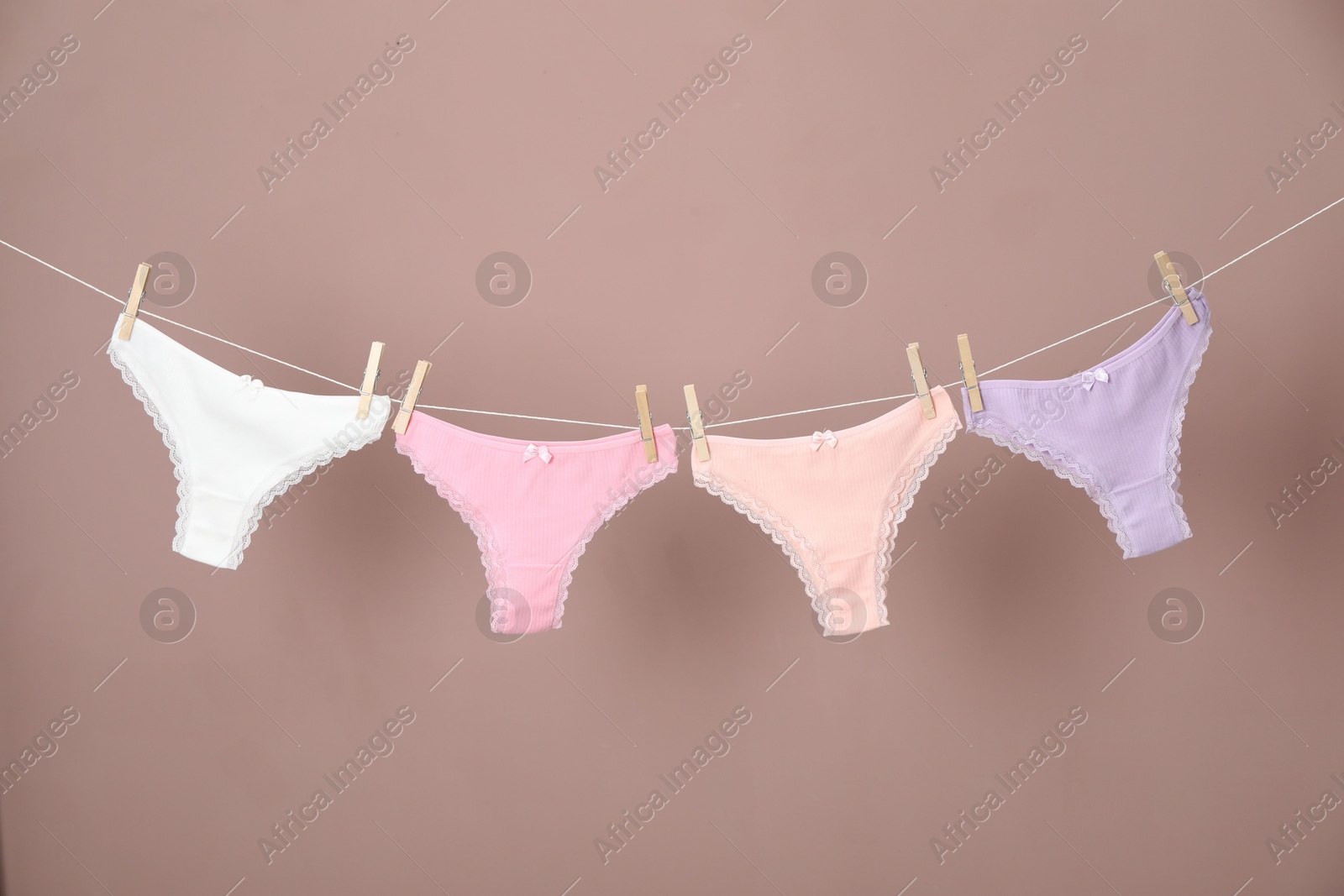 Women's underwear. Beautiful panties on clothes line against light brown background Photo of Women's underwear. Beautiful panties on clothes line against light brown background