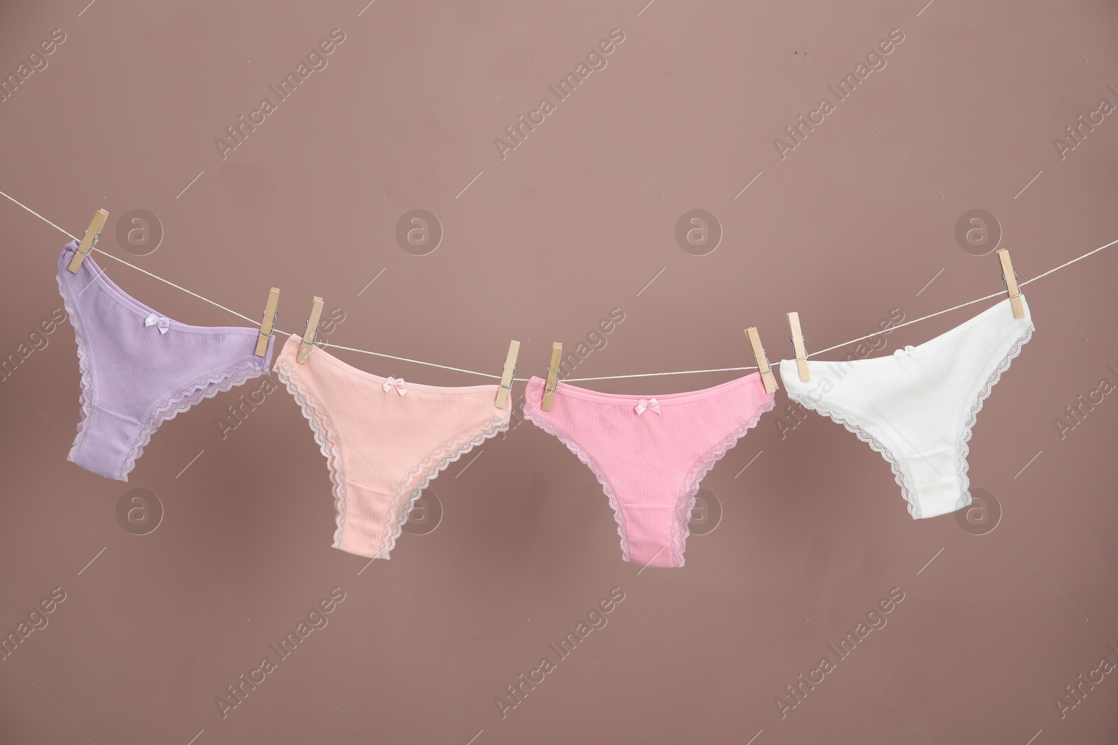 Women's underwear. Beautiful panties on clothes line against light brown background Photo of Women's underwear. Beautiful panties on clothes line against light brown background