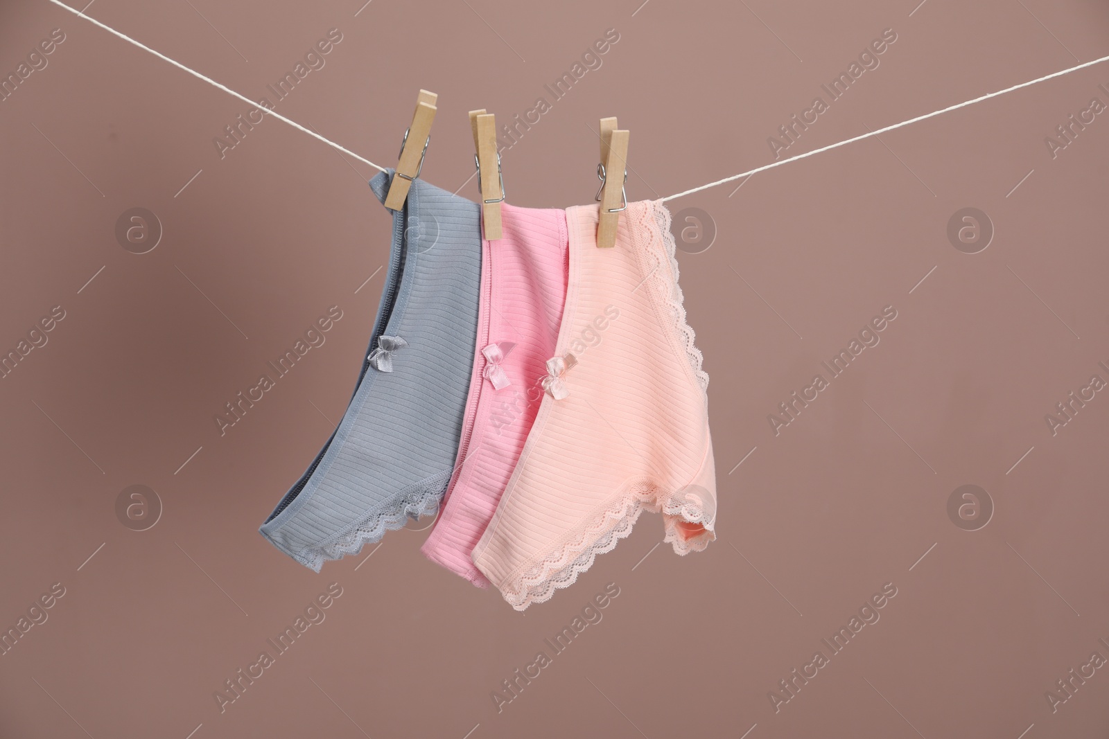 Women's underwear. Beautiful panties on clothes line against light brown background Photo of Women's underwear. Beautiful panties on clothes line against light brown background
