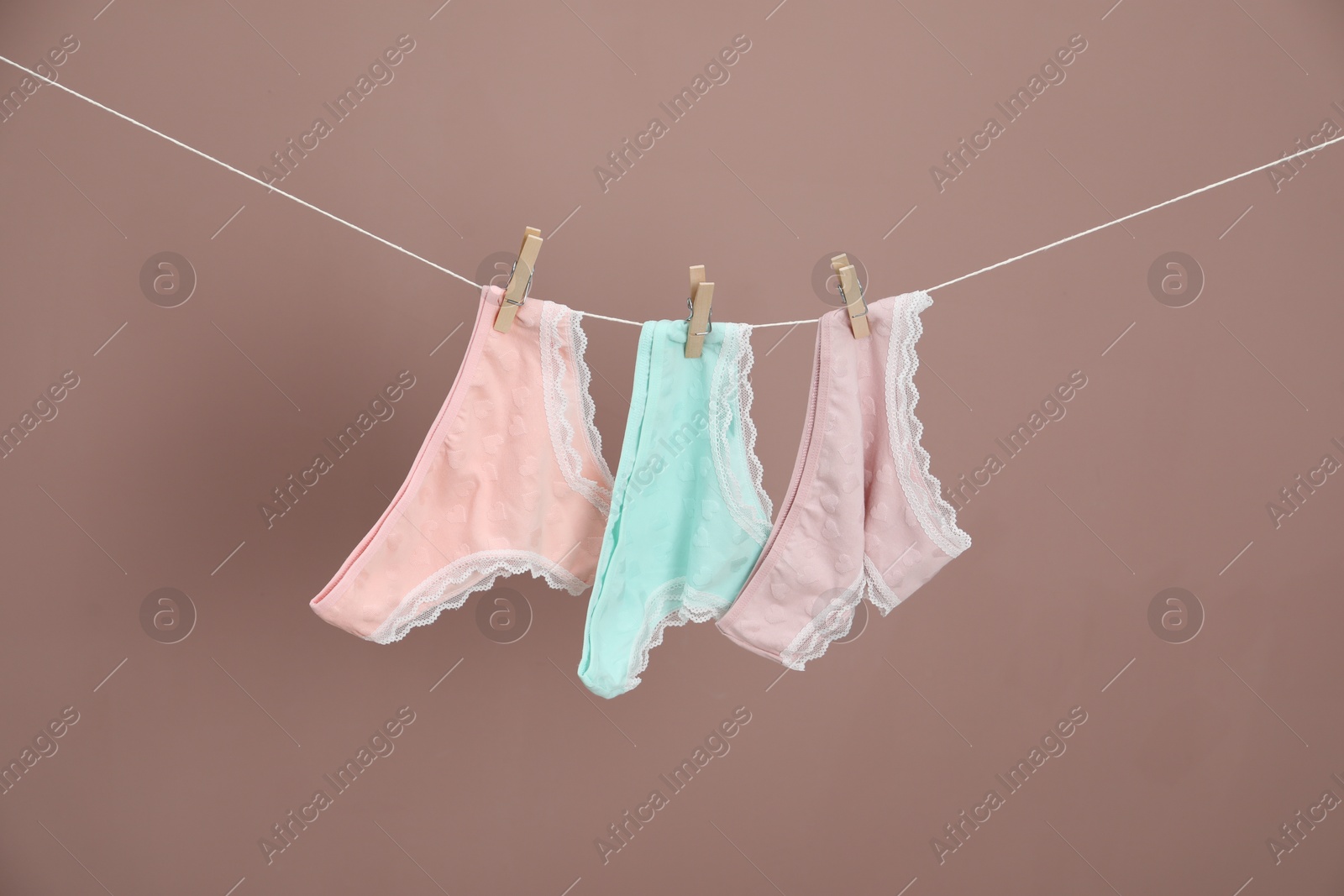 Women's underwear. Beautiful panties on clothes line against light brown background Photo of Women's underwear. Beautiful panties on clothes line against light brown background