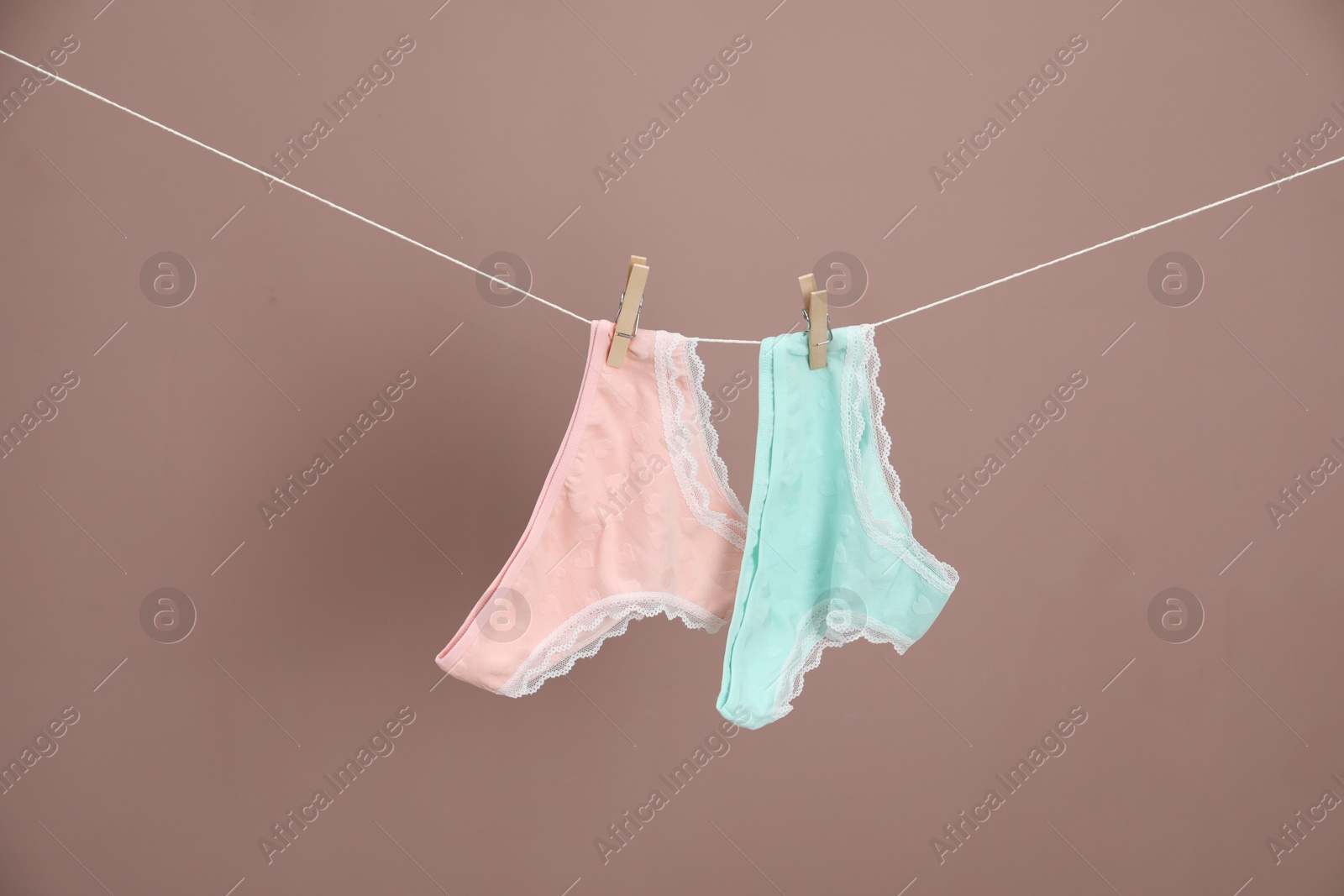 Women's underwear. Beautiful panties on clothes line against light brown background Photo of Women's underwear. Beautiful panties on clothes line against light brown background