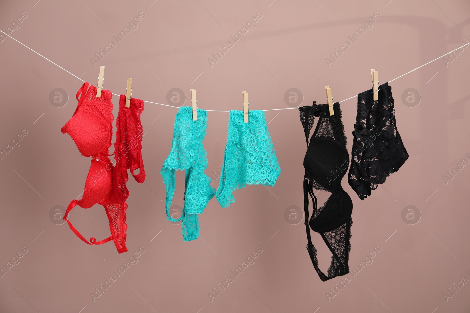 Women's underwear. Beautiful panties and bras on clothes line against light brown background Photo of Women's underwear. Beautiful panties and bras on clothes line against light brown background