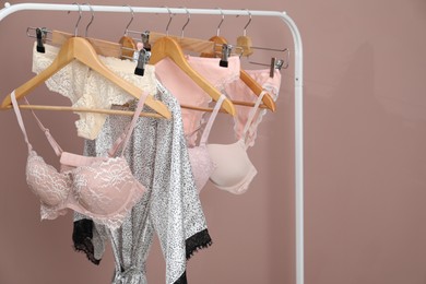 Photo of Women's underwear. Hangers with beautiful panties, bras and robe on rack against light brown background
