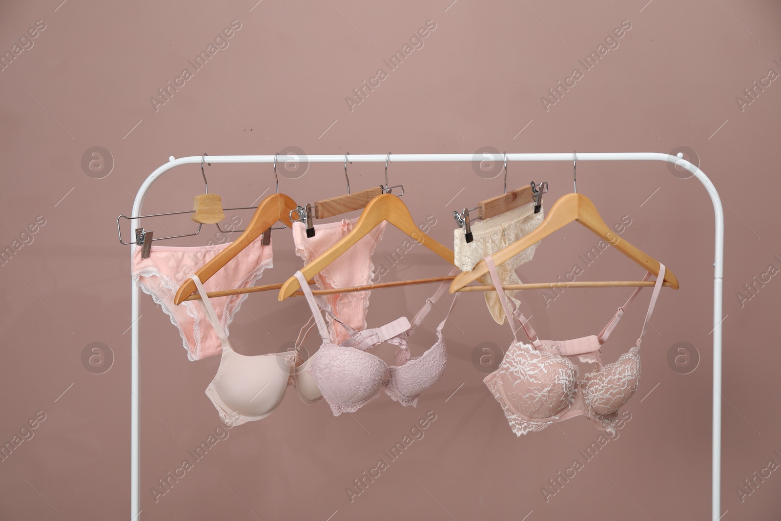 Women's underwear. Hangers with beautiful panties and bras on rack against light brown background Photo of Women's underwear. Hangers with beautiful panties and bras on rack against light brown background