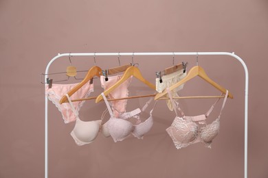 Photo of Women's underwear. Hangers with beautiful panties and bras on rack against light brown background