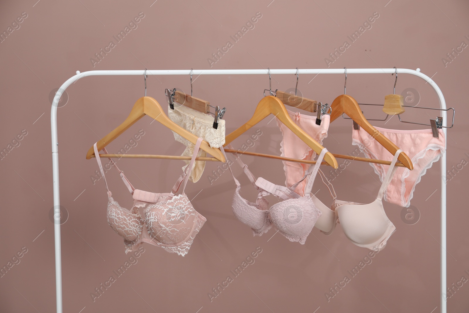 Women's underwear. Hangers with beautiful panties and bras on rack against light brown background Photo of Women's underwear. Hangers with beautiful panties and bras on rack against light brown background