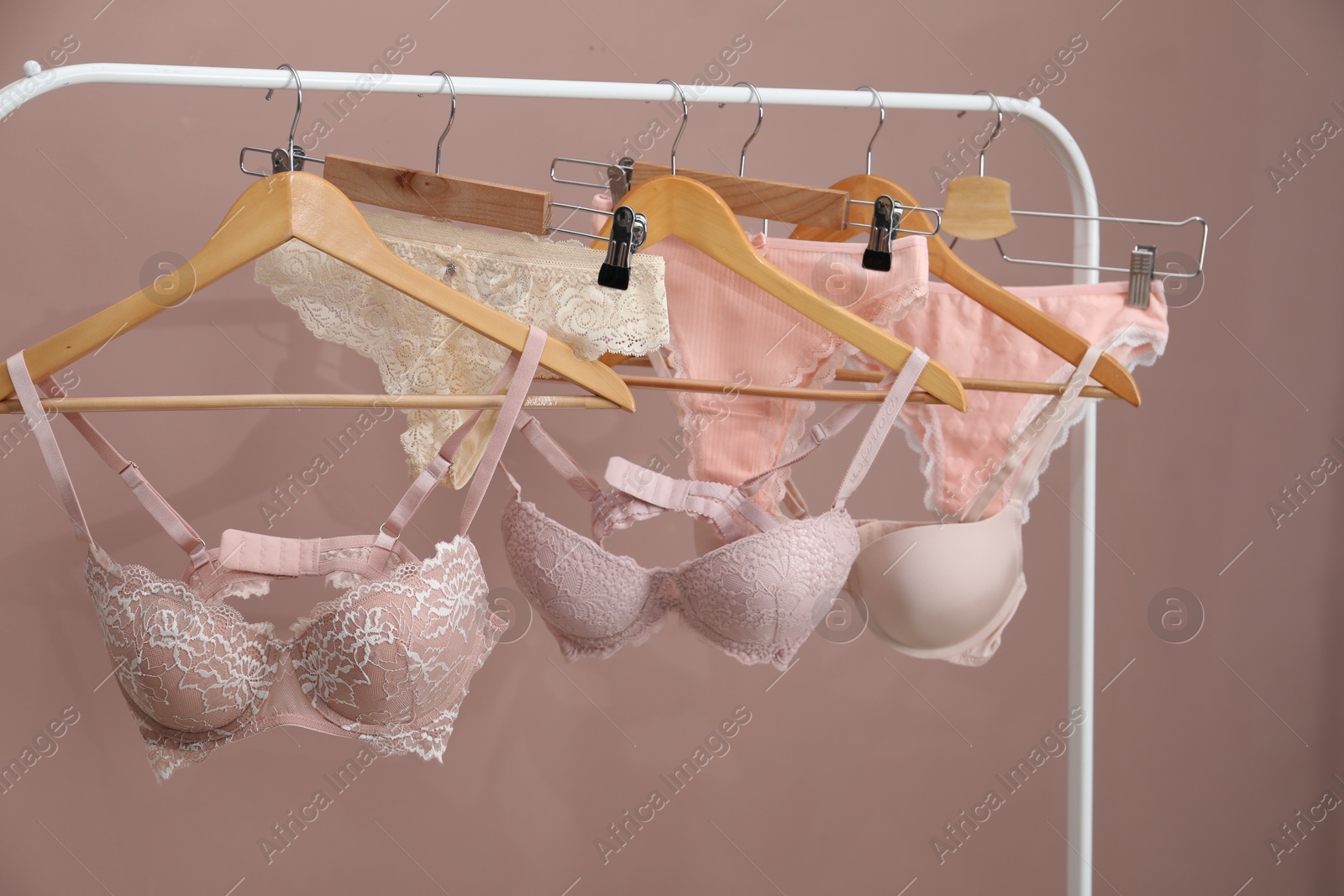 Women's underwear. Hangers with beautiful panties and bras on rack against light brown background Photo of Women's underwear. Hangers with beautiful panties and bras on rack against light brown background