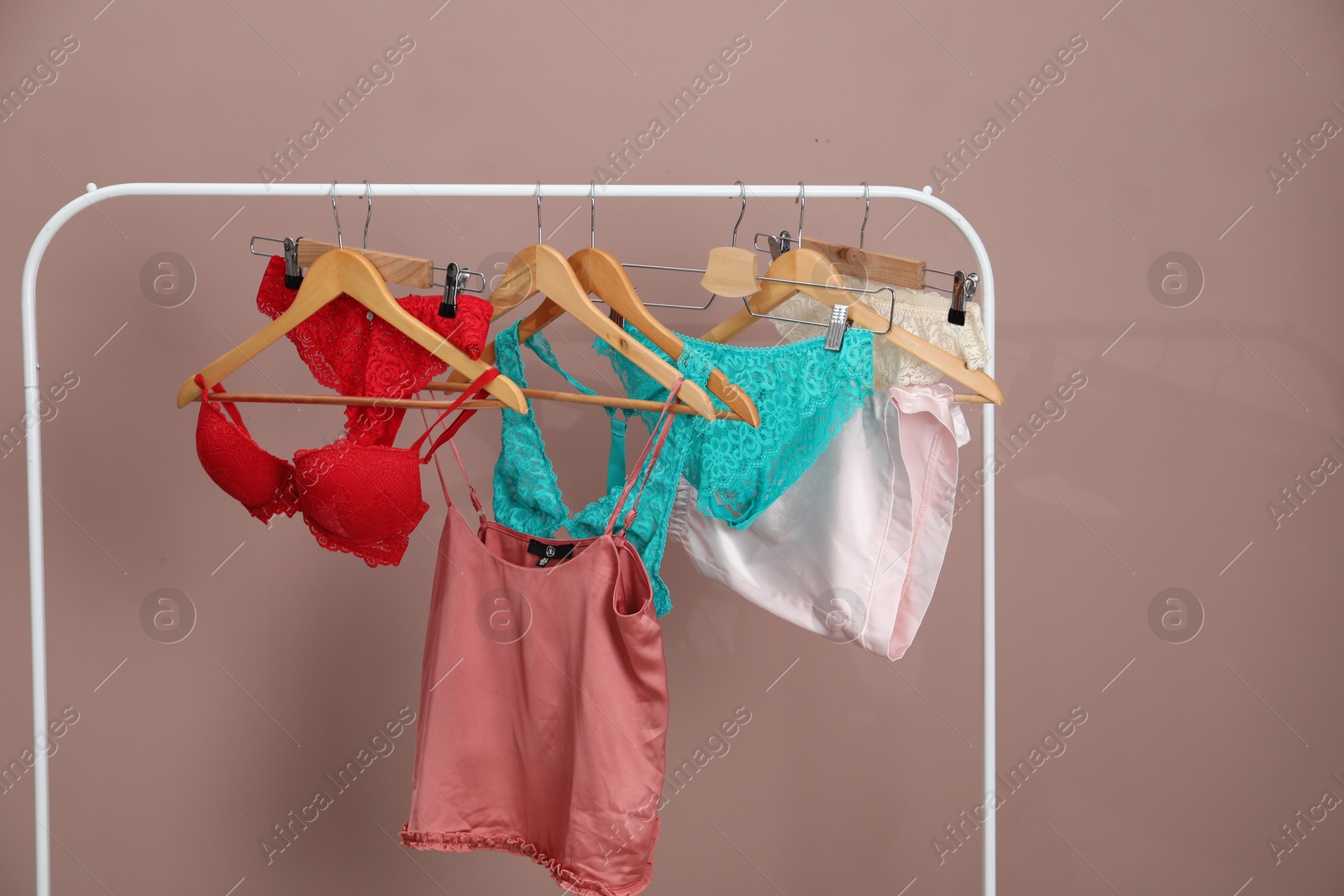 Women's underwear. Hangers with beautiful panties, bras, tank top and shorts on rack against light brown background Photo of Women's underwear. Hangers with beautiful panties, bras, tank top and shorts on rack against light brown background