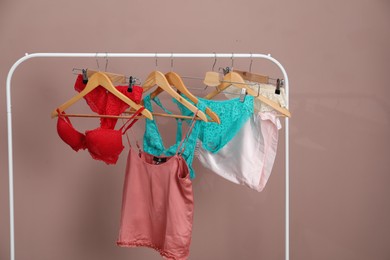 Photo of Women's underwear. Hangers with beautiful panties, bras, tank top and shorts on rack against light brown background