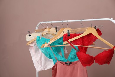 Photo of Women's underwear. Hangers with beautiful panties, bras, tank top and shorts on rack against light brown background