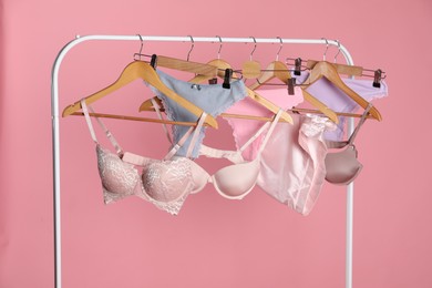 Photo of Women's underwear. Hangers with beautiful panties and bras on rack against pink background