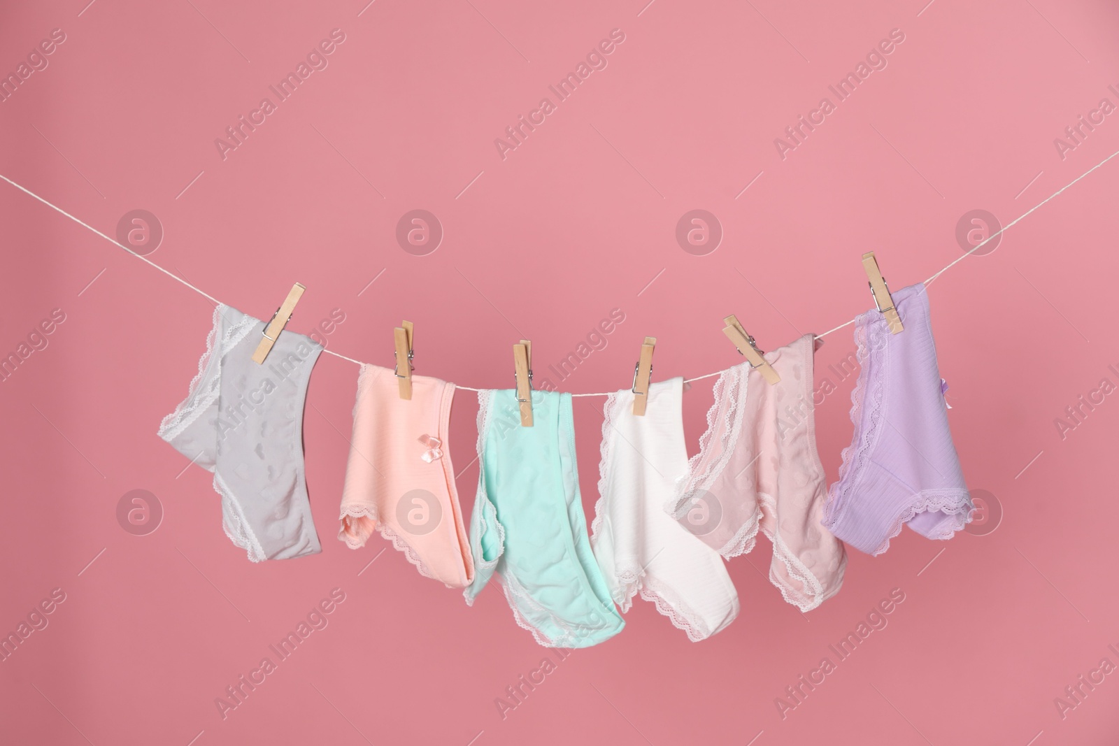 Women's underwear. Beautiful panties on clothes line against pink background Photo of Women's underwear. Beautiful panties on clothes line against pink background