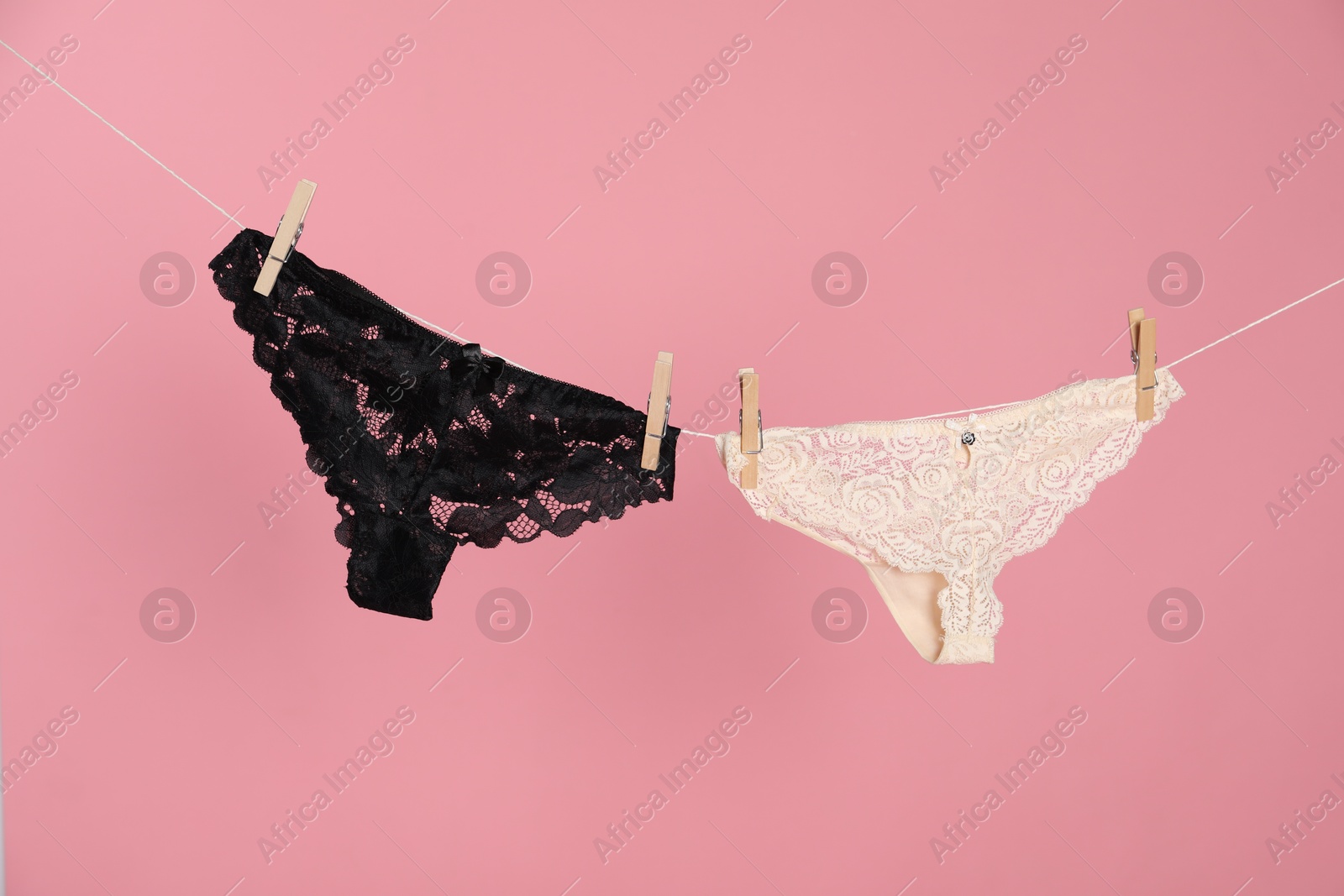 Women's underwear. Beautiful panties on clothes line against pink background Photo of Women's underwear. Beautiful panties on clothes line against pink background