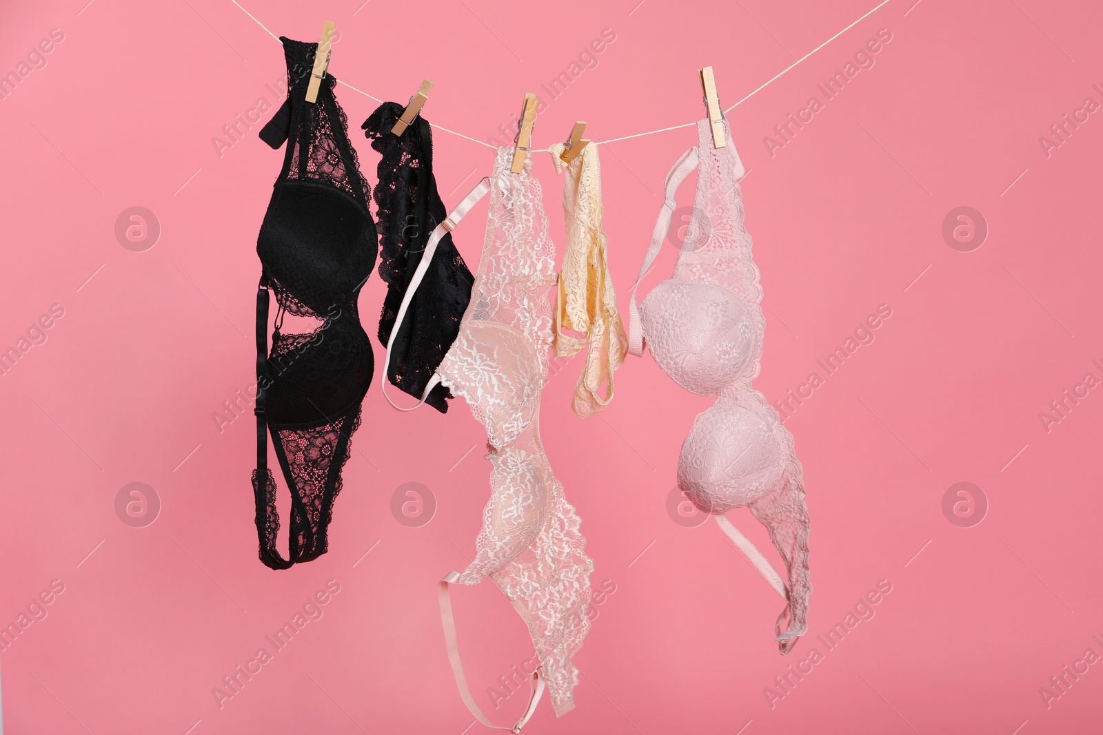 Women's underwear. Beautiful panties and bras on clothes line against pink background Photo of Women's underwear. Beautiful panties and bras on clothes line against pink background