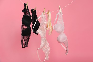 Photo of Women's underwear. Beautiful panties and bras on clothes line against pink background
