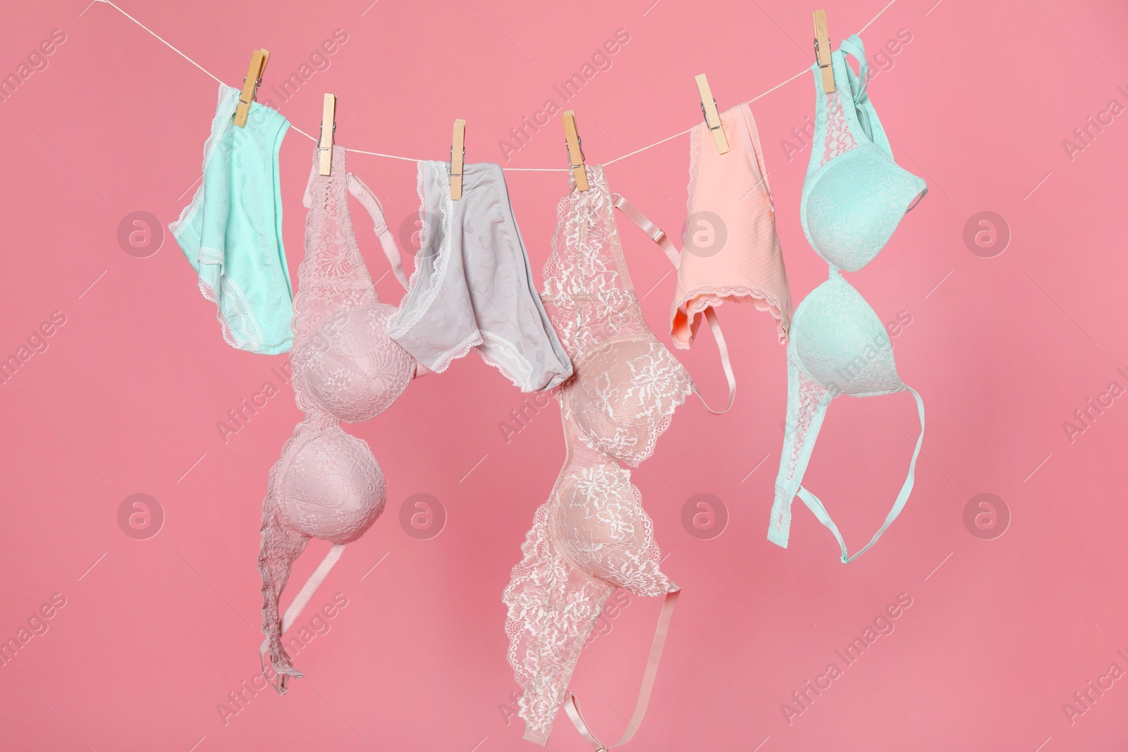 Women's underwear. Beautiful panties and bras on clothes line against pink background Photo of Women's underwear. Beautiful panties and bras on clothes line against pink background