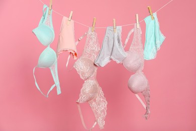 Photo of Women's underwear. Beautiful panties and bras on clothes line against pink background