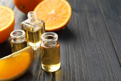 Photo of Open perfume bottles with aromatic essential oils and slices of oranges on black wooden table, closeup. Space for text