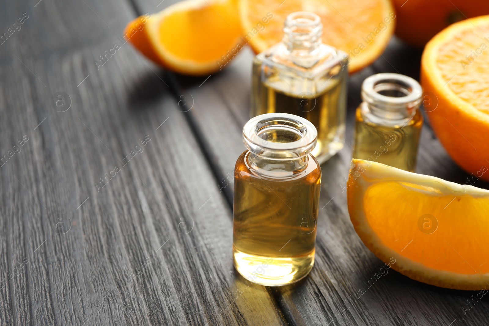 Photo of Open perfume bottles with aromatic essential oils and slices of oranges on black wooden table, closeup. Space for text