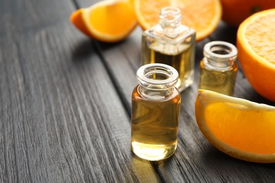 Photo of Open perfume bottles with aromatic essential oils and slices of oranges on black wooden table, closeup. Space for text