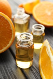 Photo of Open perfume bottles with aromatic essential oils and slices of oranges on black wooden table, closeup