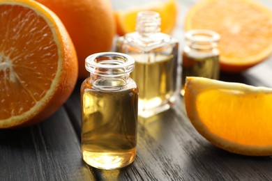 Photo of Open perfume bottles with aromatic essential oils and slices of oranges on black wooden table, closeup