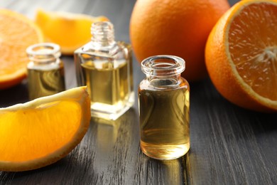 Photo of Open perfume bottles with aromatic essential oils and slices of oranges on black wooden table, closeup