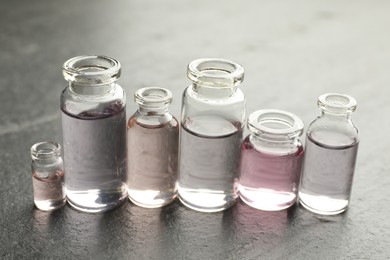 Photo of Open perfume bottles with aromatic essential oils on dark textured table, closeup