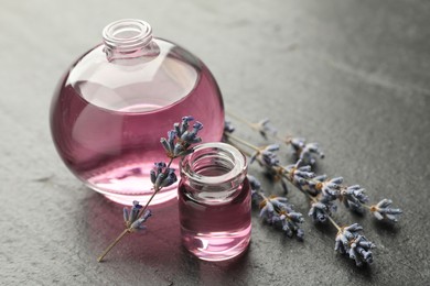 Photo of Open perfume bottles with aromatic essential oils and lavender branches on dark textured table, closeup