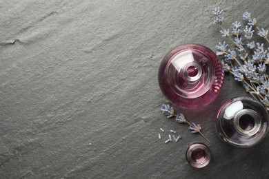 Photo of Open perfume bottles with aromatic essential oils and lavender branches on dark textured table, flat lay. Space for text
