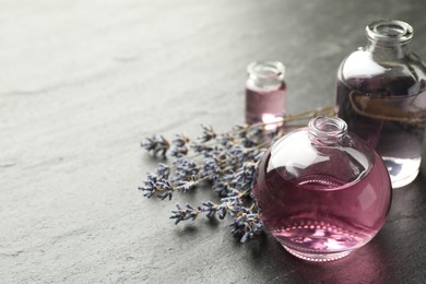 Photo of Open perfume bottles with aromatic essential oils and lavender branches on dark textured table, closeup. Space for text