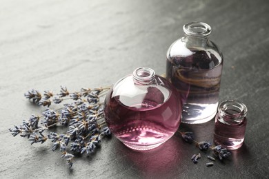 Photo of Open perfume bottles with aromatic essential oils and lavender branches on dark textured table, closeup