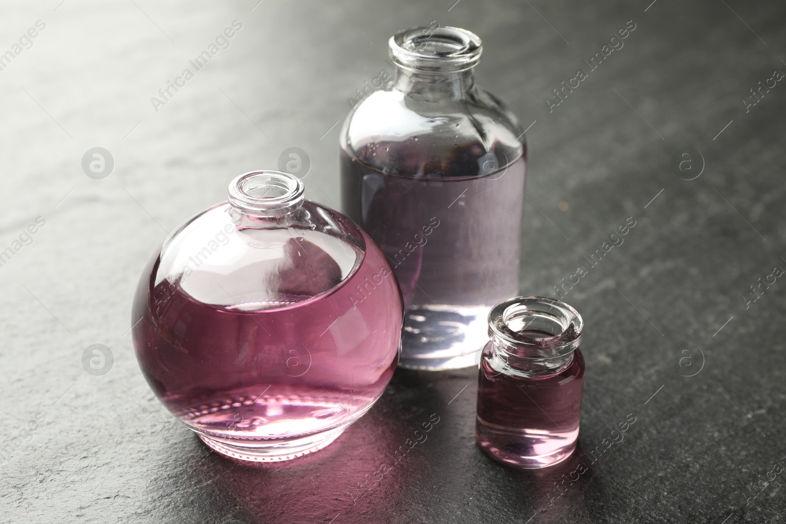 Open perfume bottles with aromatic essential oils on dark textured table, closeup Photo of Open perfume bottles with aromatic essential oils on dark textured table, closeup