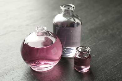 Photo of Open perfume bottles with aromatic essential oils on dark textured table, closeup