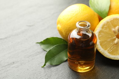 Photo of Open perfume bottle with aromatic essential oil, leaves and lemons on dark textured table, closeup. Space for text