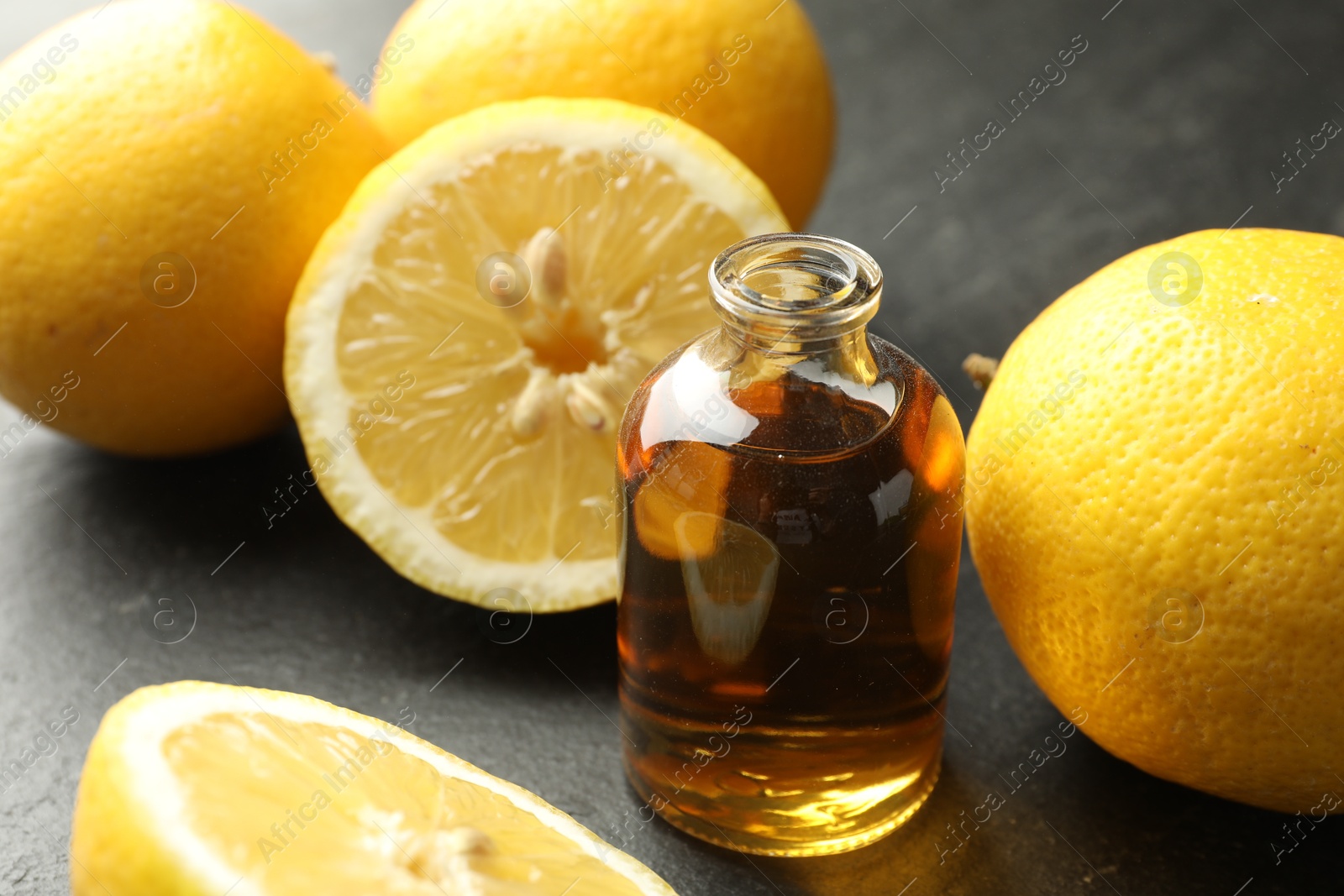 Photo of Open perfume bottle with aromatic essential oil and lemons on dark textured table, closeup