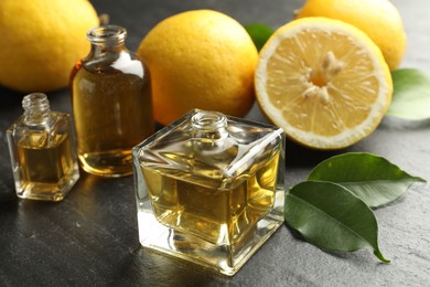 Photo of Open perfume bottles with aromatic essential oils, leaves and lemons on dark textured table, closeup