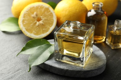 Photo of Open perfume bottles with aromatic essential oils, leaves and lemons on dark textured table, closeup